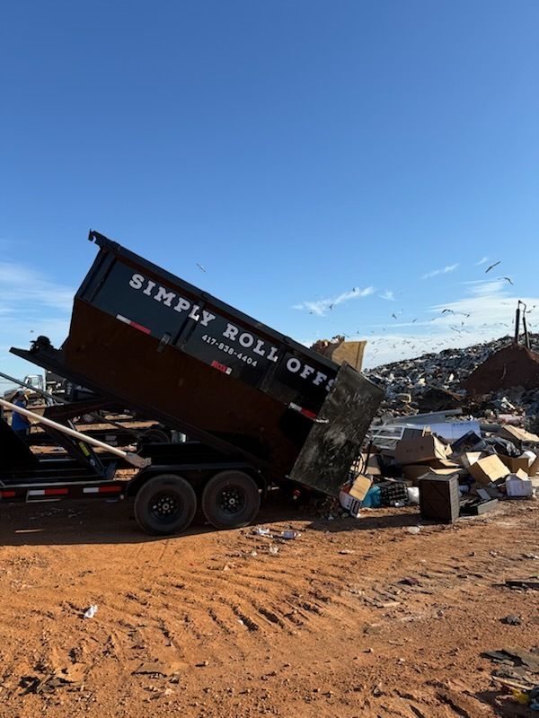 Dumpster tilted on a truck at a demolition site, with debris and dirt under a clear blue sky.