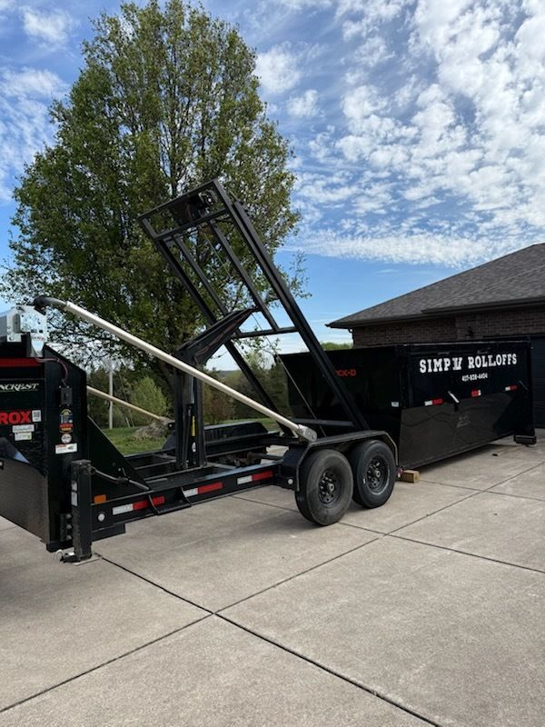 Black dump trailer with raised bed parked on a driveway under a partly cloudy sky.