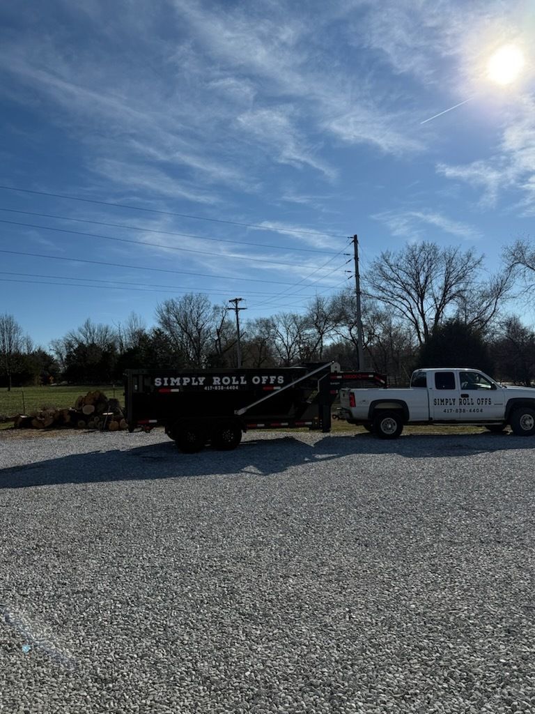 Pickup truck towing a black dump trailer on a gravel lot under a bright blue sky