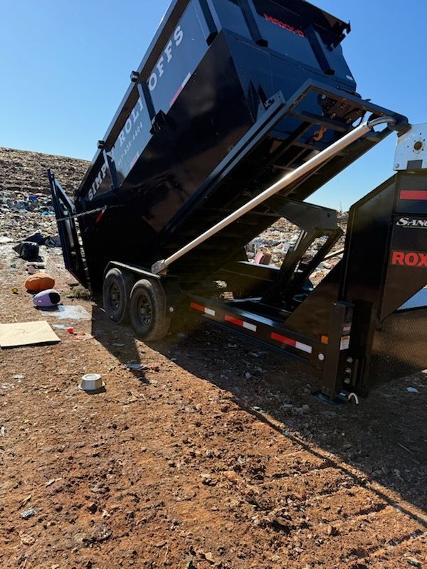Dump truck bed raised at a steep angle in a gravel lot under a clear blue sky