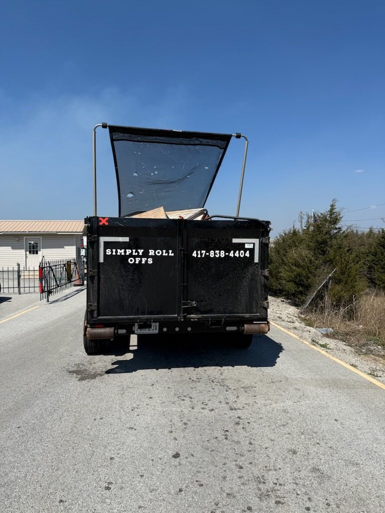Black dump truck with raised open bed parked on a road under a clear blue sky.