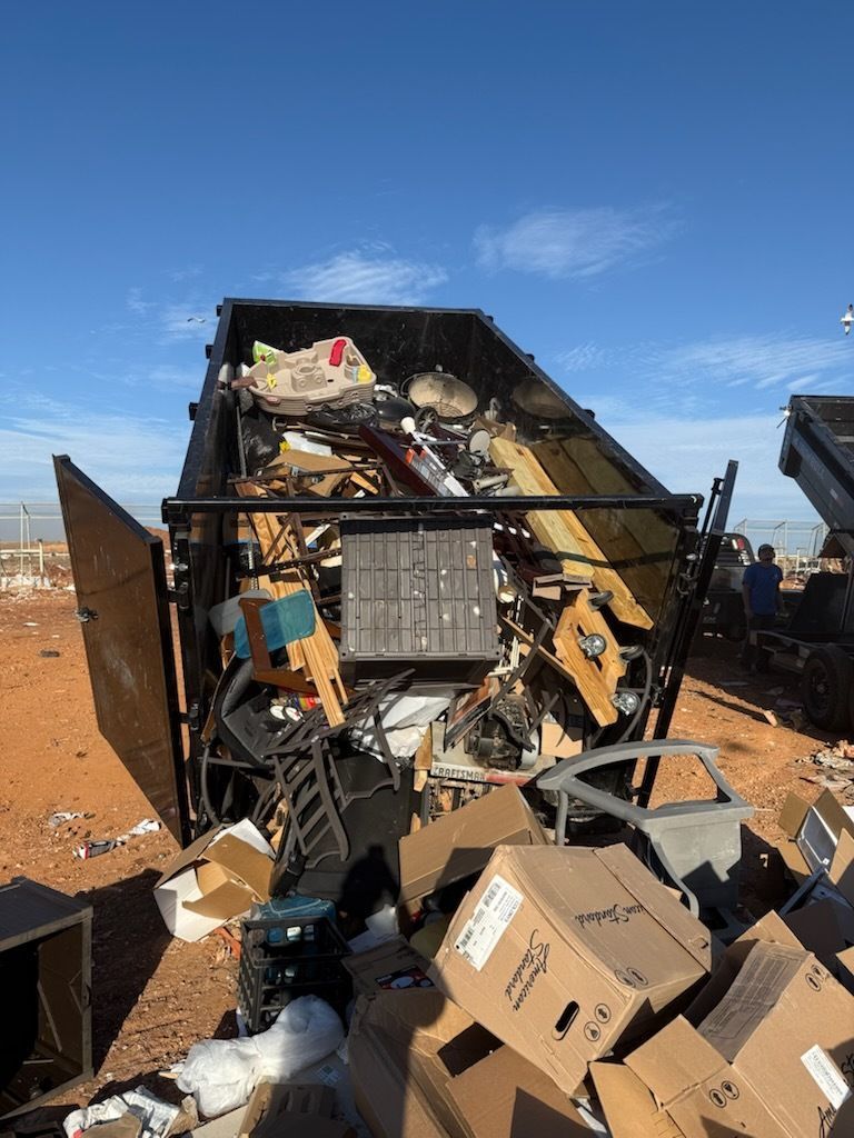 Overturned garbage truck spilling trash and cardboard in a dry, open area under a blue sky