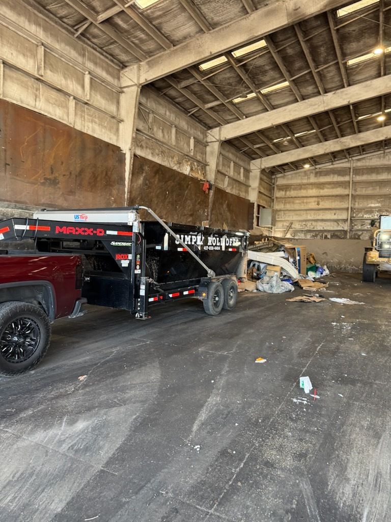 Interior of a warehouse with a black tow truck, equipment, and a dirt floor under high ceilings