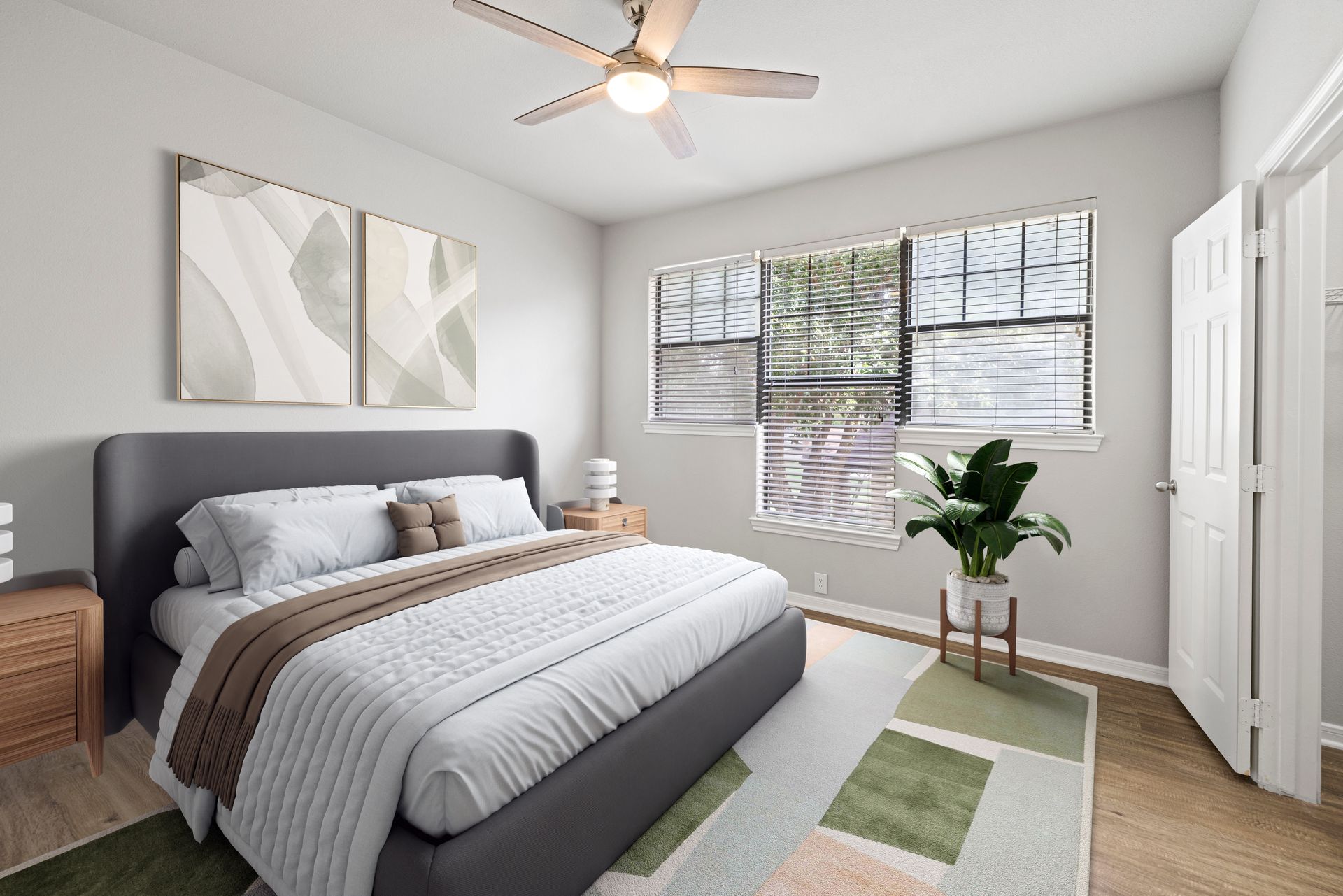Bright bedroom with gray bed, white closet, ceiling fan, and window with blinds and a plant.