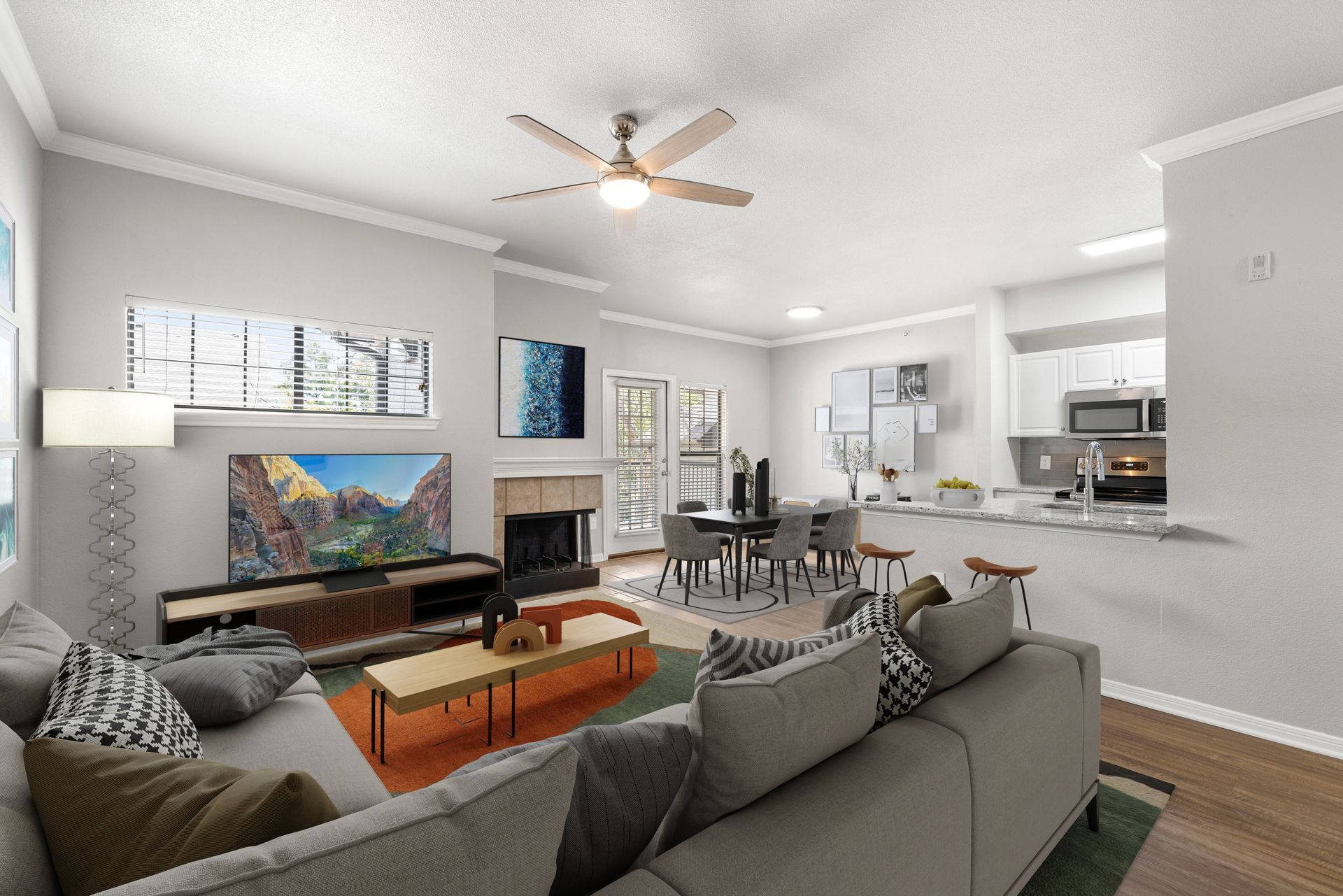 Bright living room with gray sectional, orange coffee table, fireplace, and open kitchen beyond