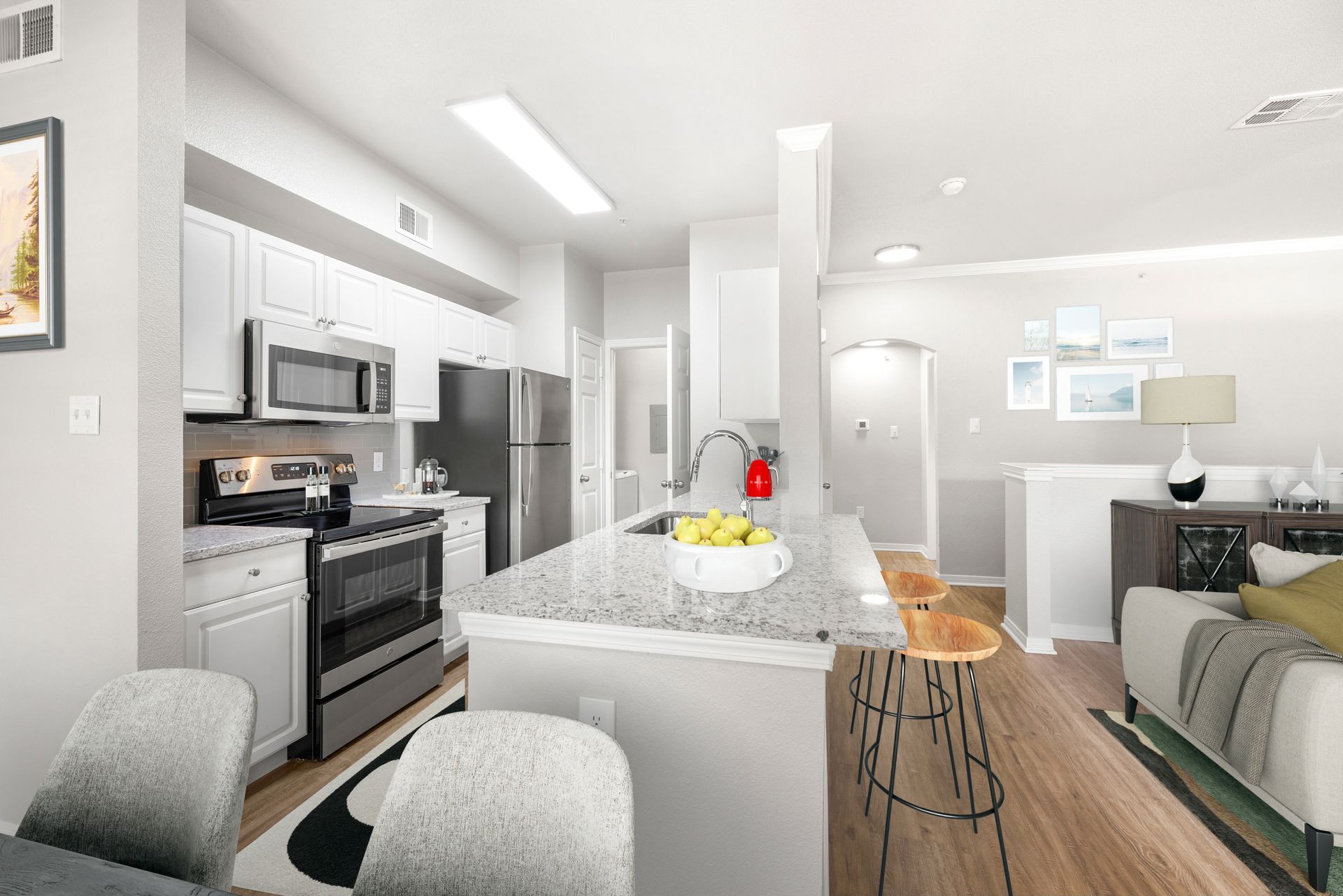 Bright modern kitchen and living room with white cabinets, island, stainless appliances, and wood floors