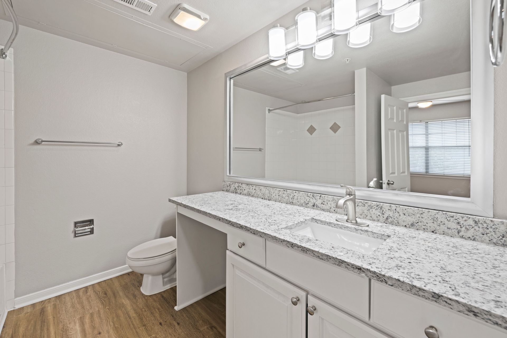 Bright bathroom with double vanity, large mirror, granite countertop, toilet, and walk-in shower.