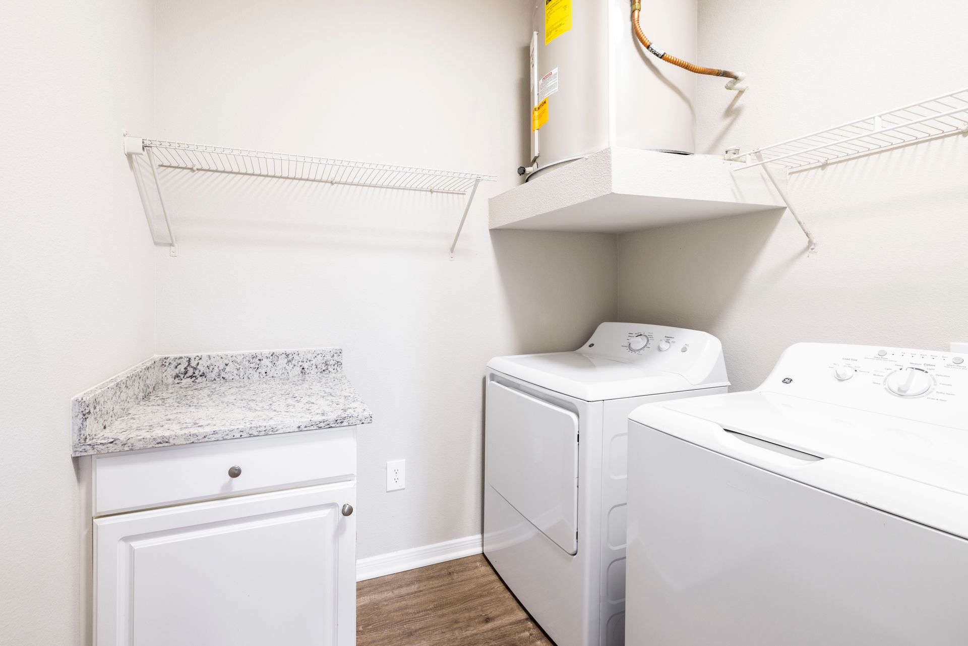 Laundry room with white washer and dryer, utility sink, and overhead shelving on tiled floor.