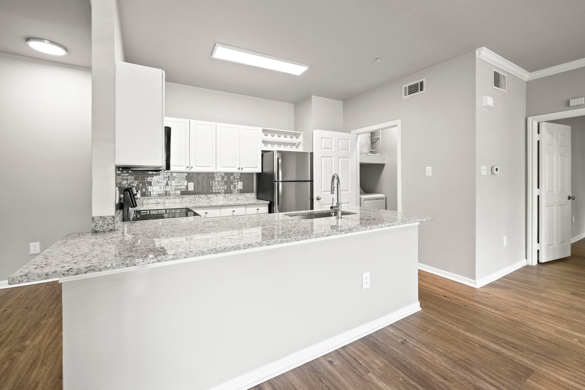 Bright open kitchen with white cabinets, granite island, stainless appliances, and wood floors
