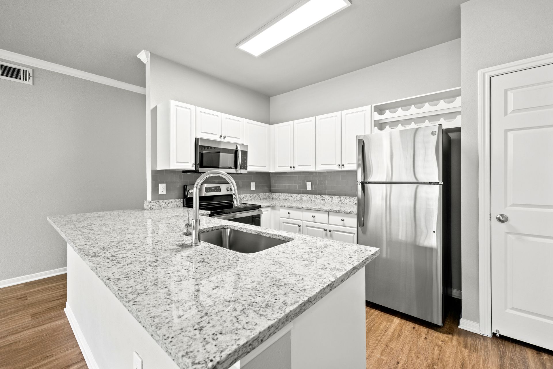 Bright modern kitchen with white cabinets, granite island, stainless steel appliances, and hardwood floors