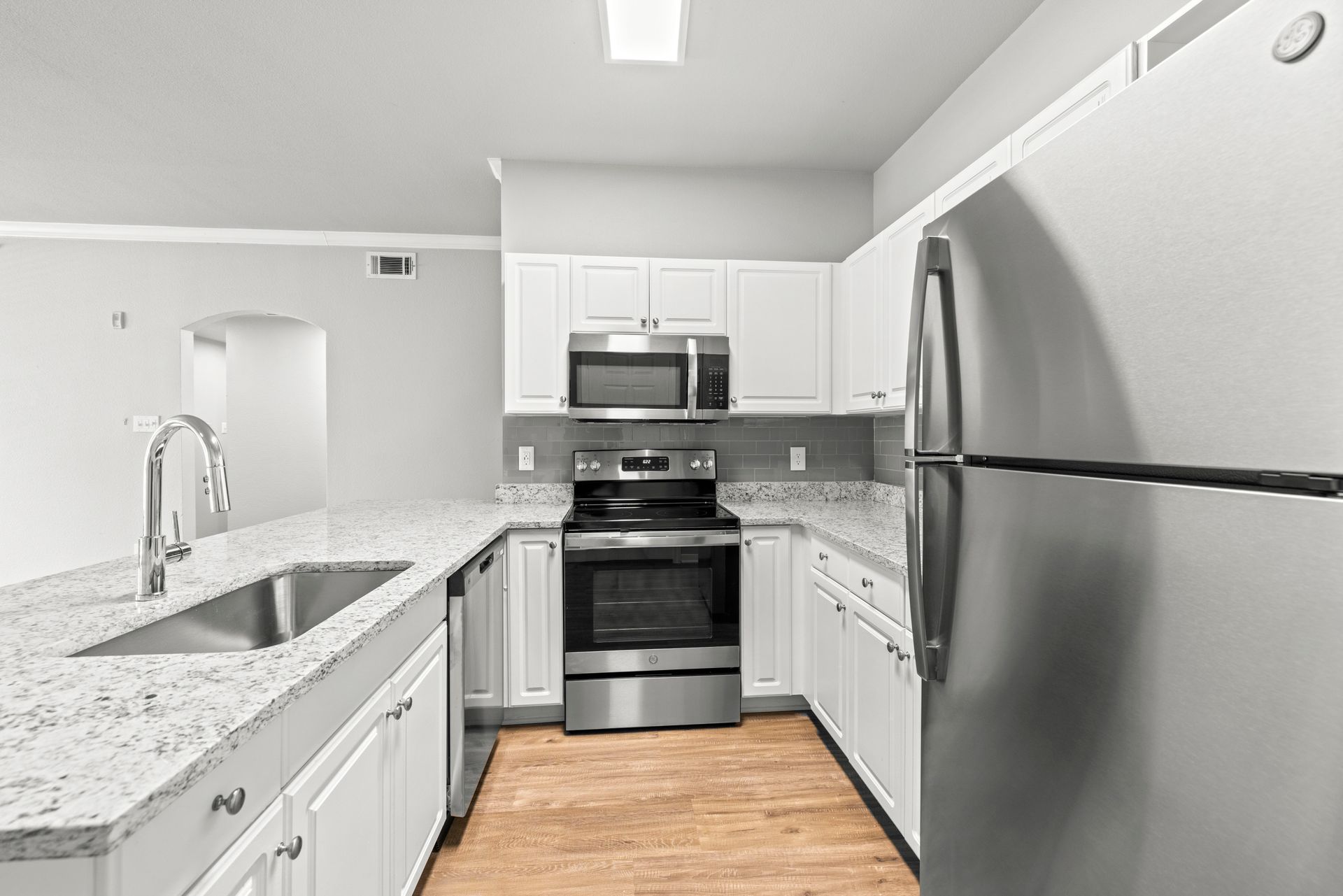 Bright white modern kitchen with stainless steel appliances, marble countertops, and wood flooring
