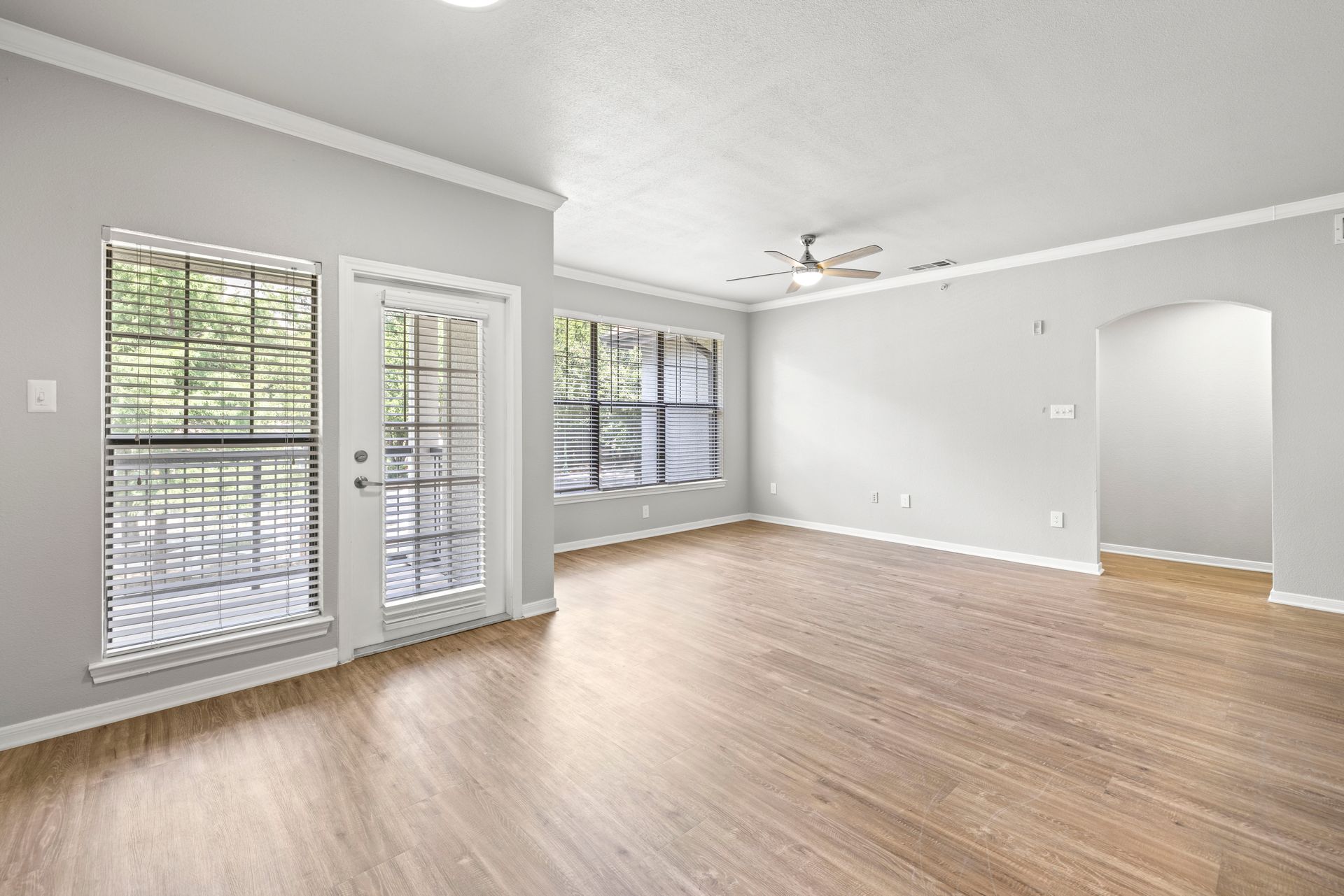 Bright empty living room with wood floors, gray walls, and large windows with blinds