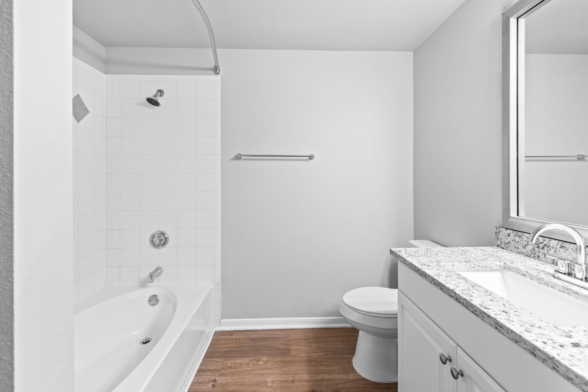 Bright bathroom with tub, toilet, and vanity sink on wood-look floor.