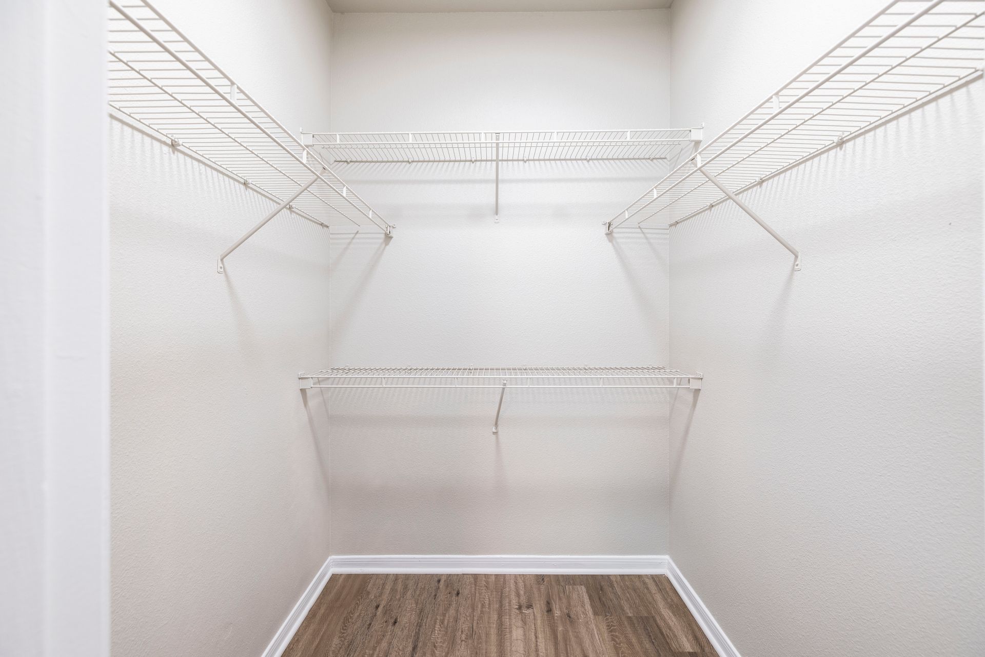 Empty walk-in closet with white wire shelving and wood flooring