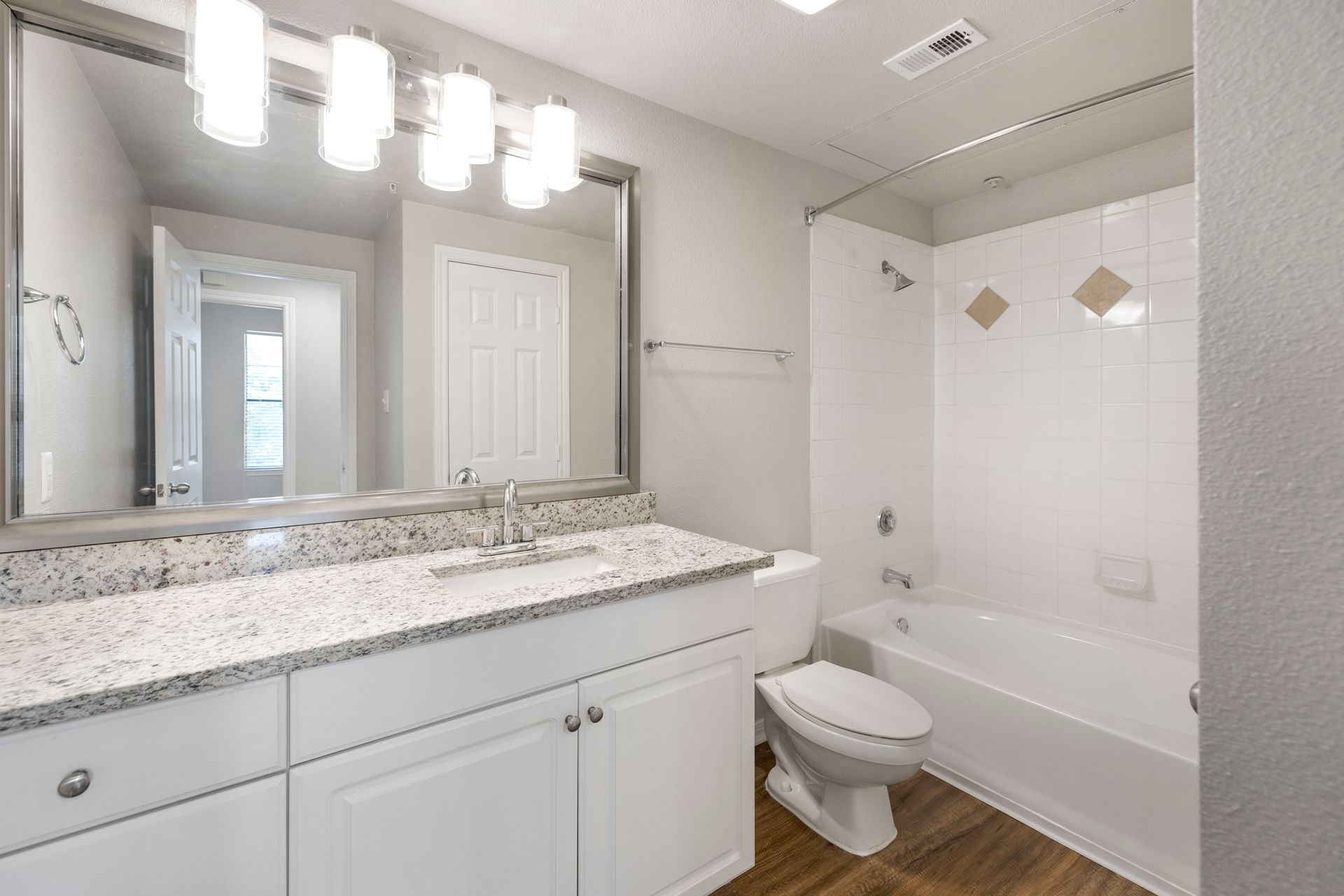 Bright modern bathroom with double vanity, granite countertop, mirror, tub-shower, and white fixtures.