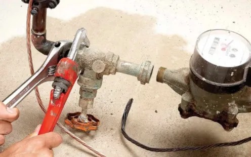 GTZ Plumbing Service LLC - A person is fixing a water meter with a wrench.