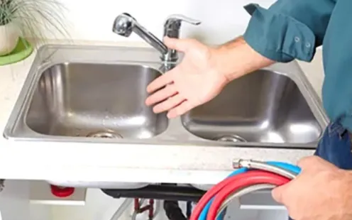 GTZ Plumbing Service LLC - A plumber is fixing a kitchen sink with a hose.