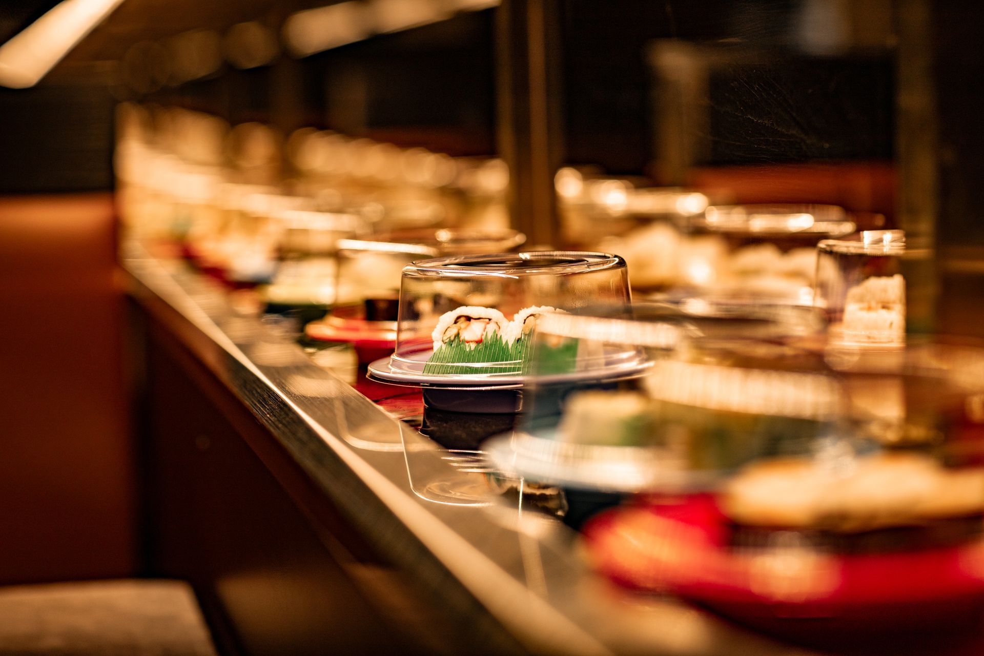 Sushi dishes on a conveyor belt at a restaurant, with various rolls displayed on colorful plates.