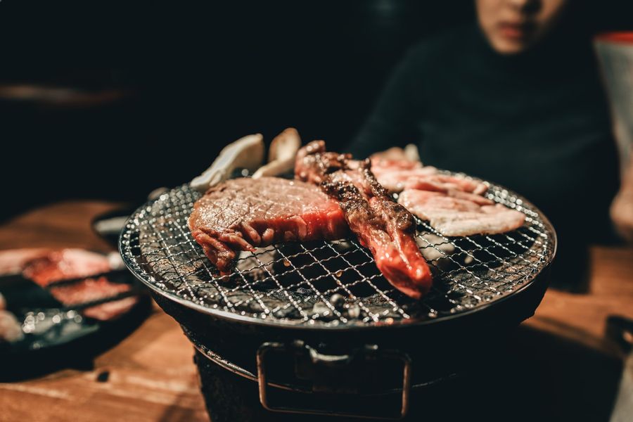 Close-up of grilled meat on a small charcoal grill at a restaurant. A person sits blurred in the background.