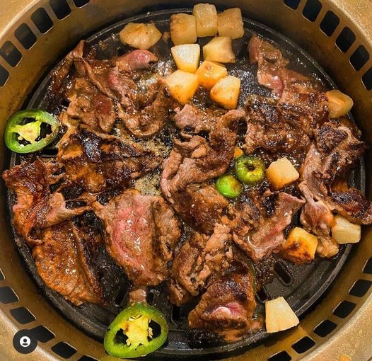 Grilled meat and potatoes on a hot plate with jalapeño slices, likely at a Korean BBQ restaurant.