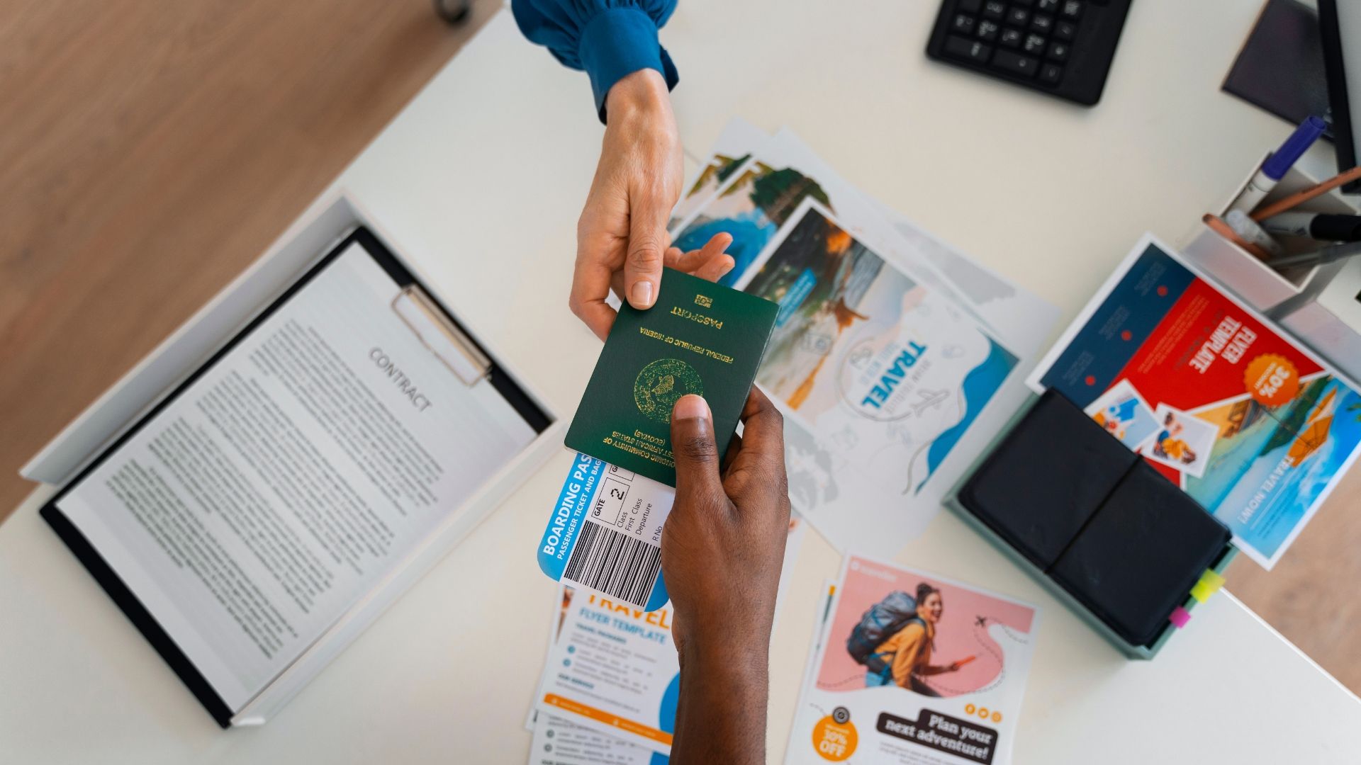 Hands exchanging a green passport over a desk with documents and travel brochures.