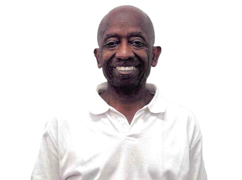 Bald man with brown skin, smiling, wearing a white polo shirt, against a white backdrop.