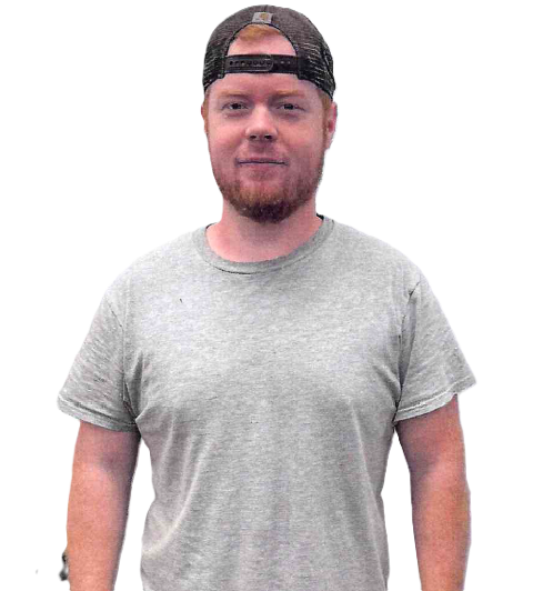 Man with red beard and baseball cap wearing a gray t-shirt, standing.