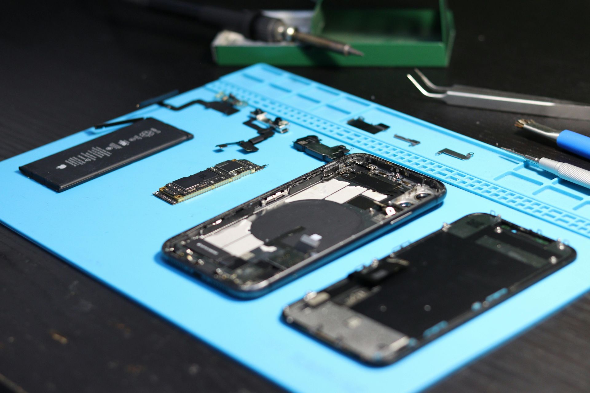 Disassembled phone on a blue mat with tools and components. Black phone frame next to a screen, battery, and other parts.