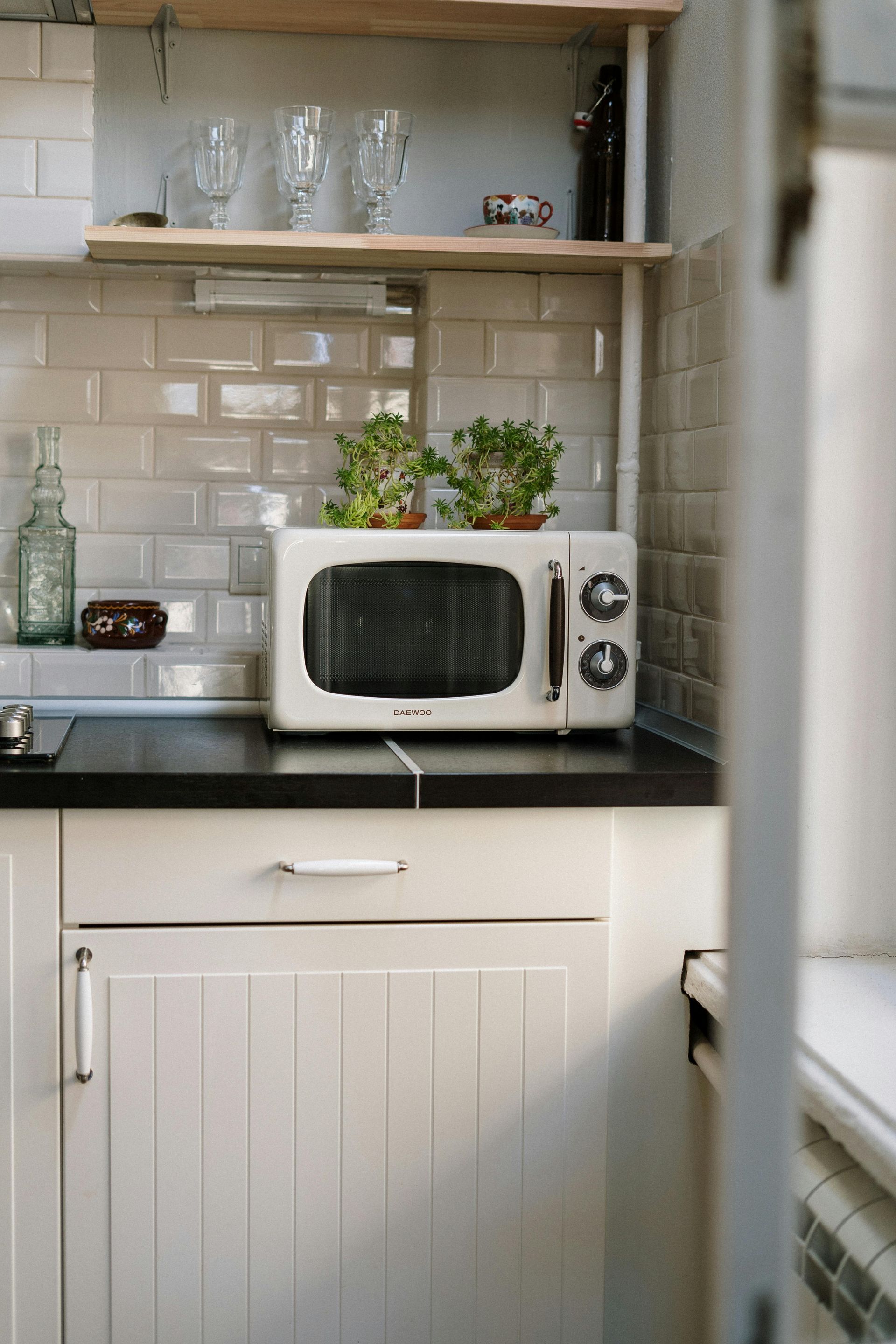 White microwave on black countertop in a small kitchen. Plants on top of the microwave.
