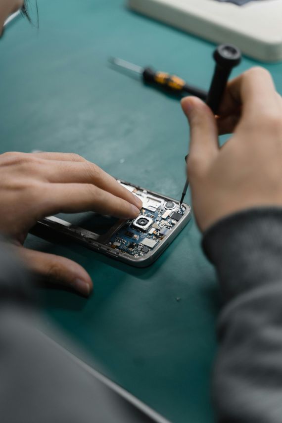 Hands repairing a disassembled mobile phone with small tools on a green surface.
