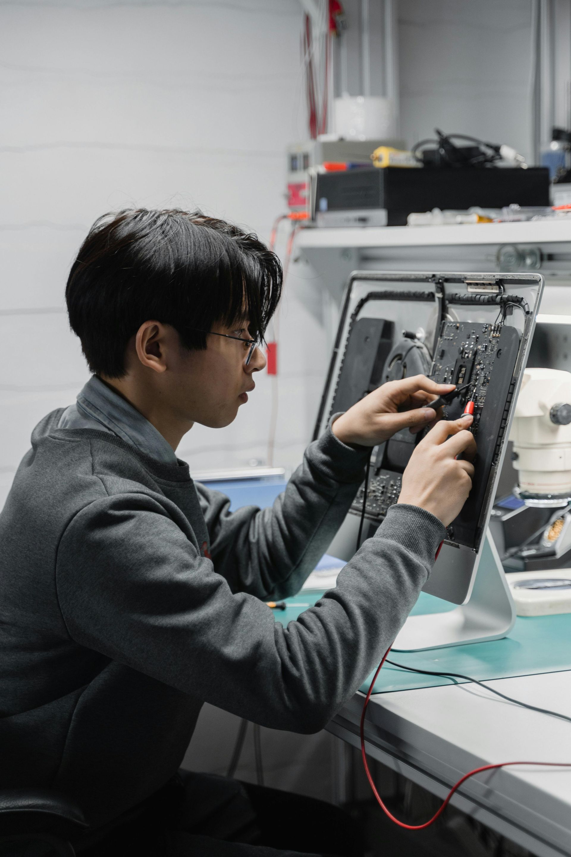 Man working on a computer circuit board with tools. He sits at a desk in a tech workshop.
