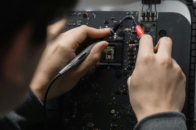 Hands using probes to test a circuit board, likely for repair.