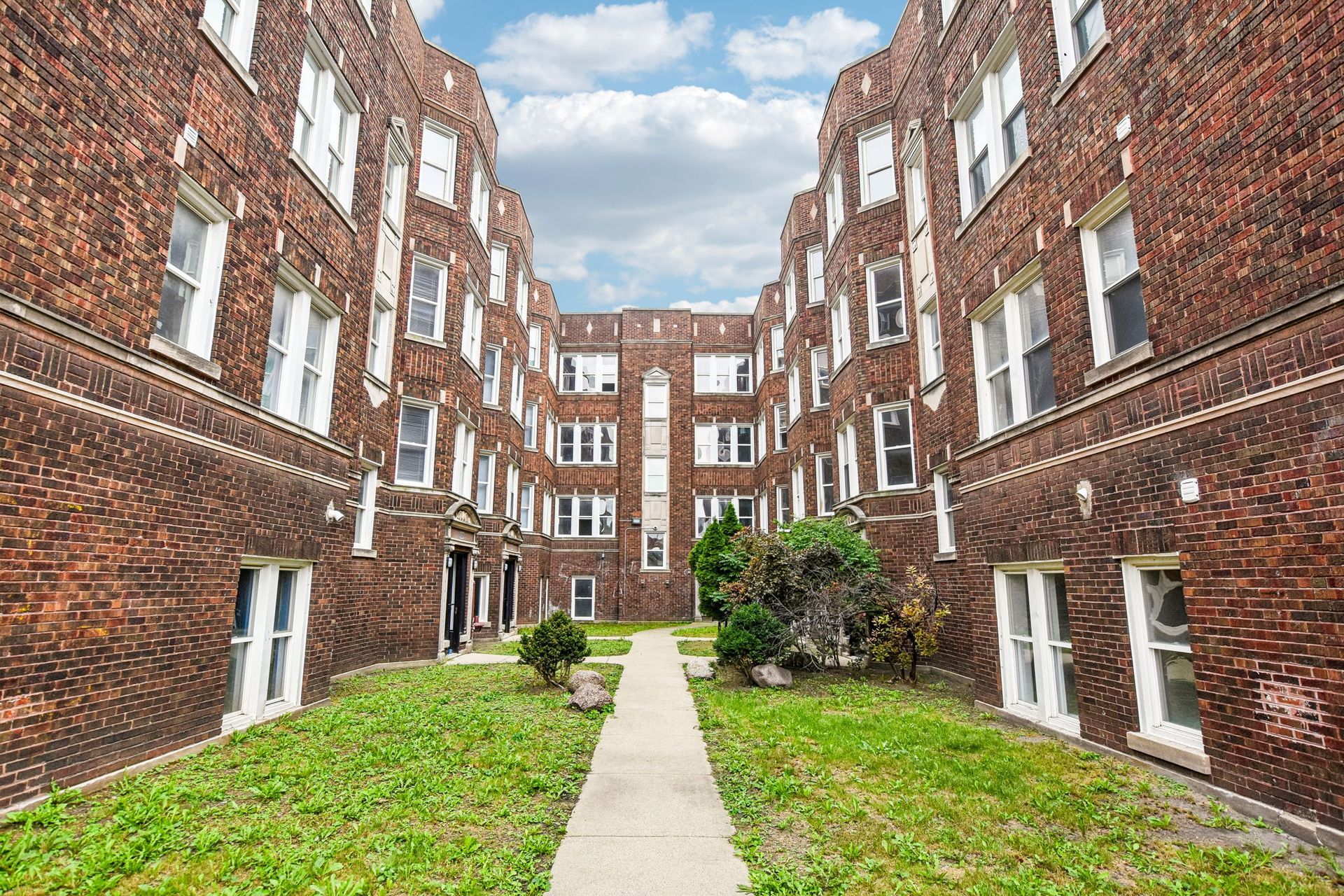 Brick apartment courtyard with grass, central walkway, and surrounding red-brick buildings.