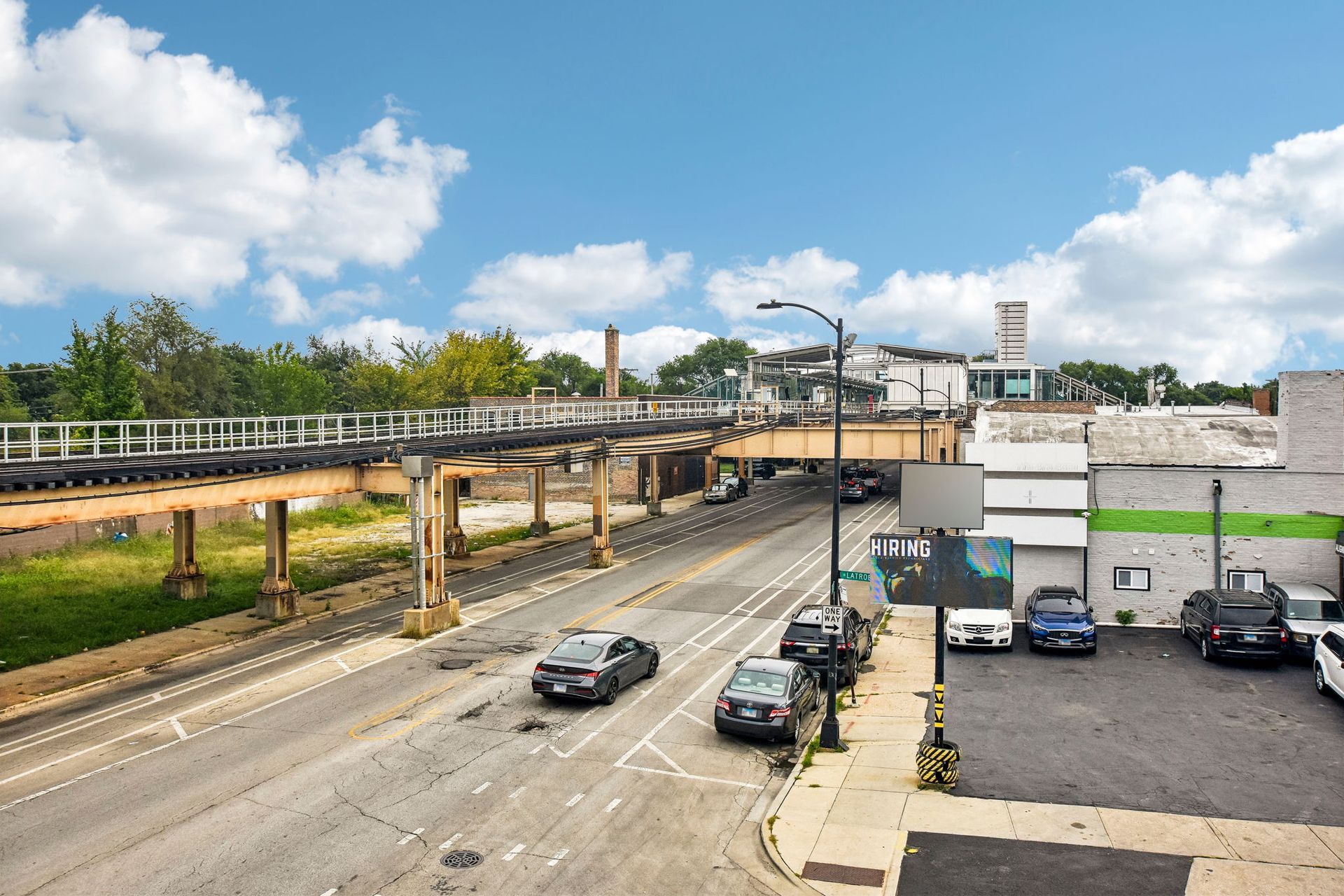 Elevated walkway over a city street with cars and a small parking lot under a blue sky