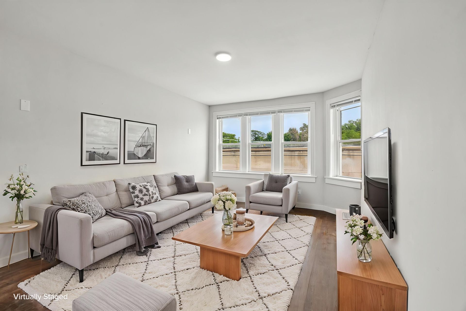 Bright modern living room with gray sofa, armchair, coffee table, rug, and large bay window.