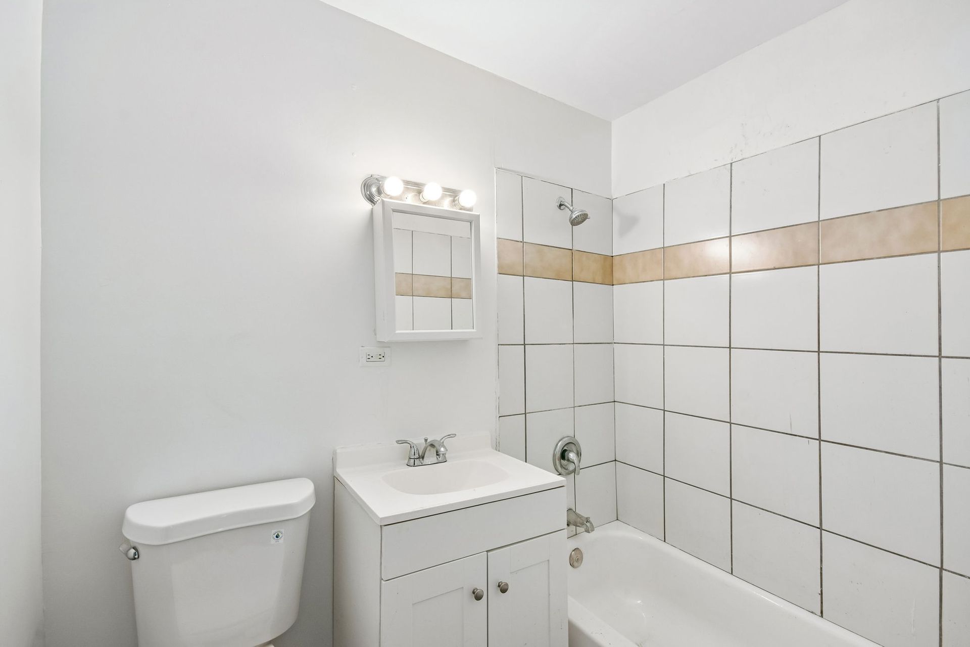 Small white bathroom with toilet, sink, mirror, and tiled shower tub.