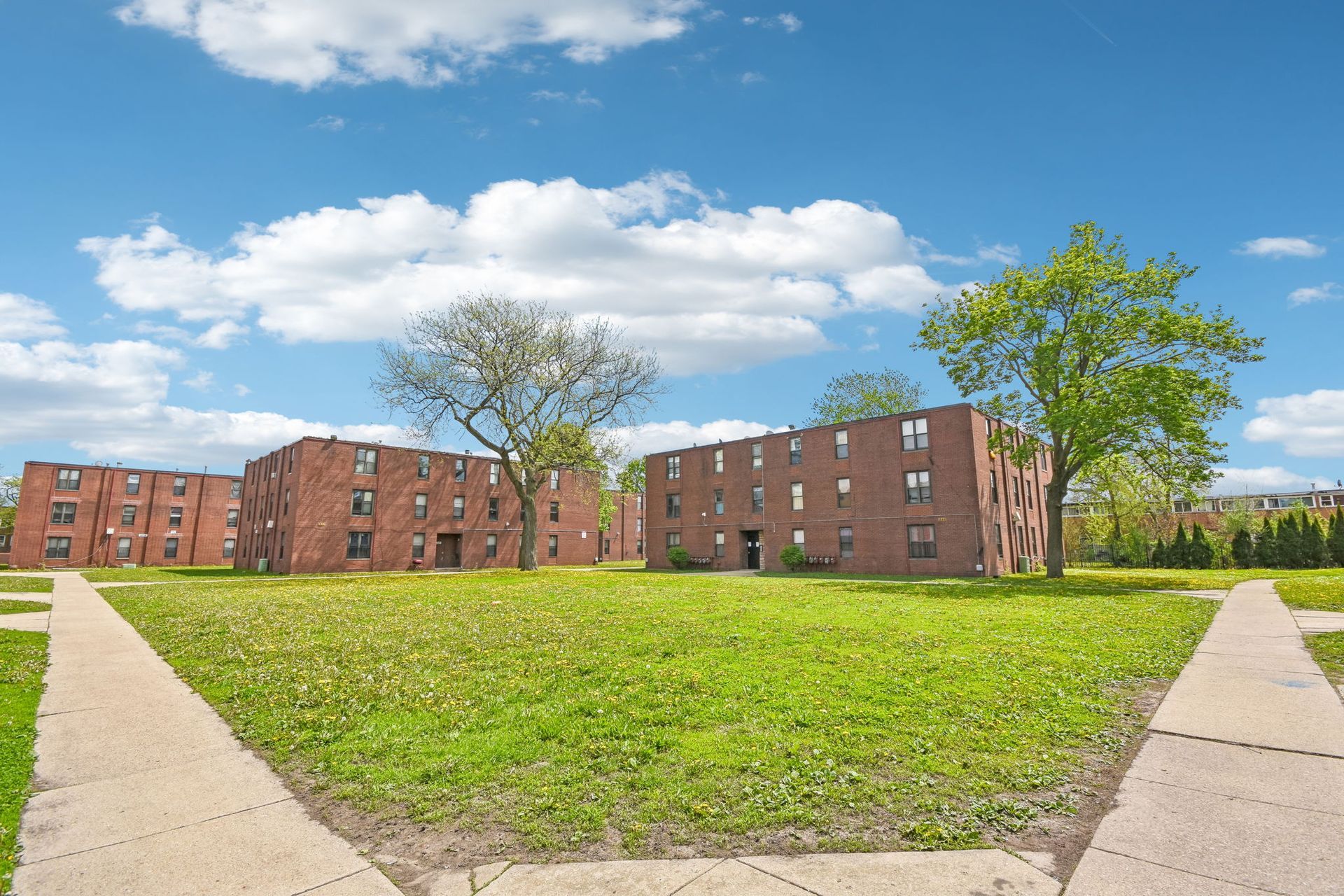 Brick apartment buildings across a grassy courtyard under a blue sky with clouds