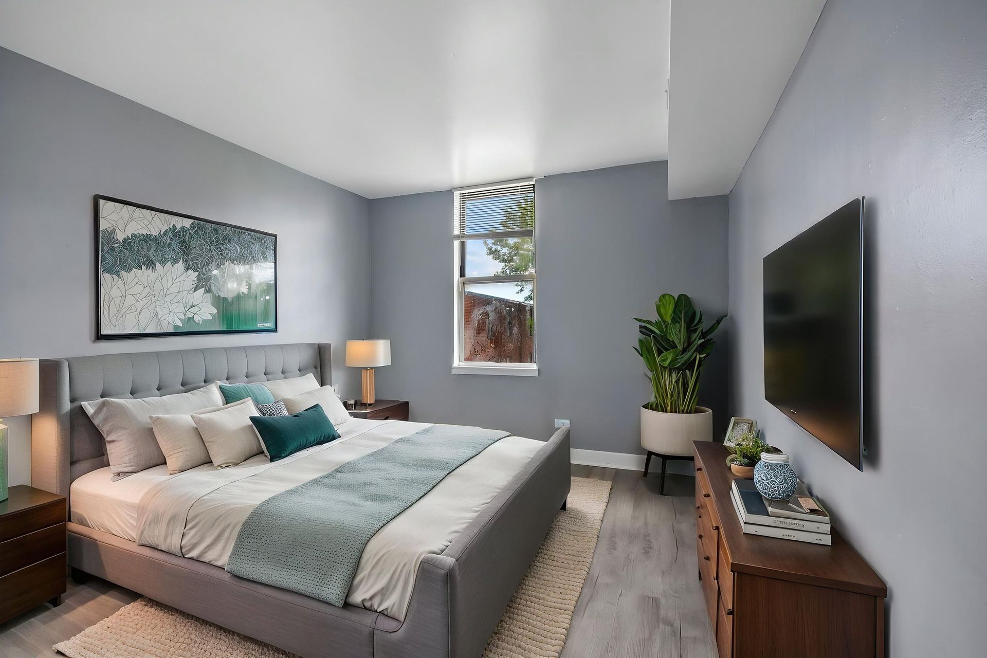 Bright modern bedroom with a neatly made bed, wall art, TV, and plants