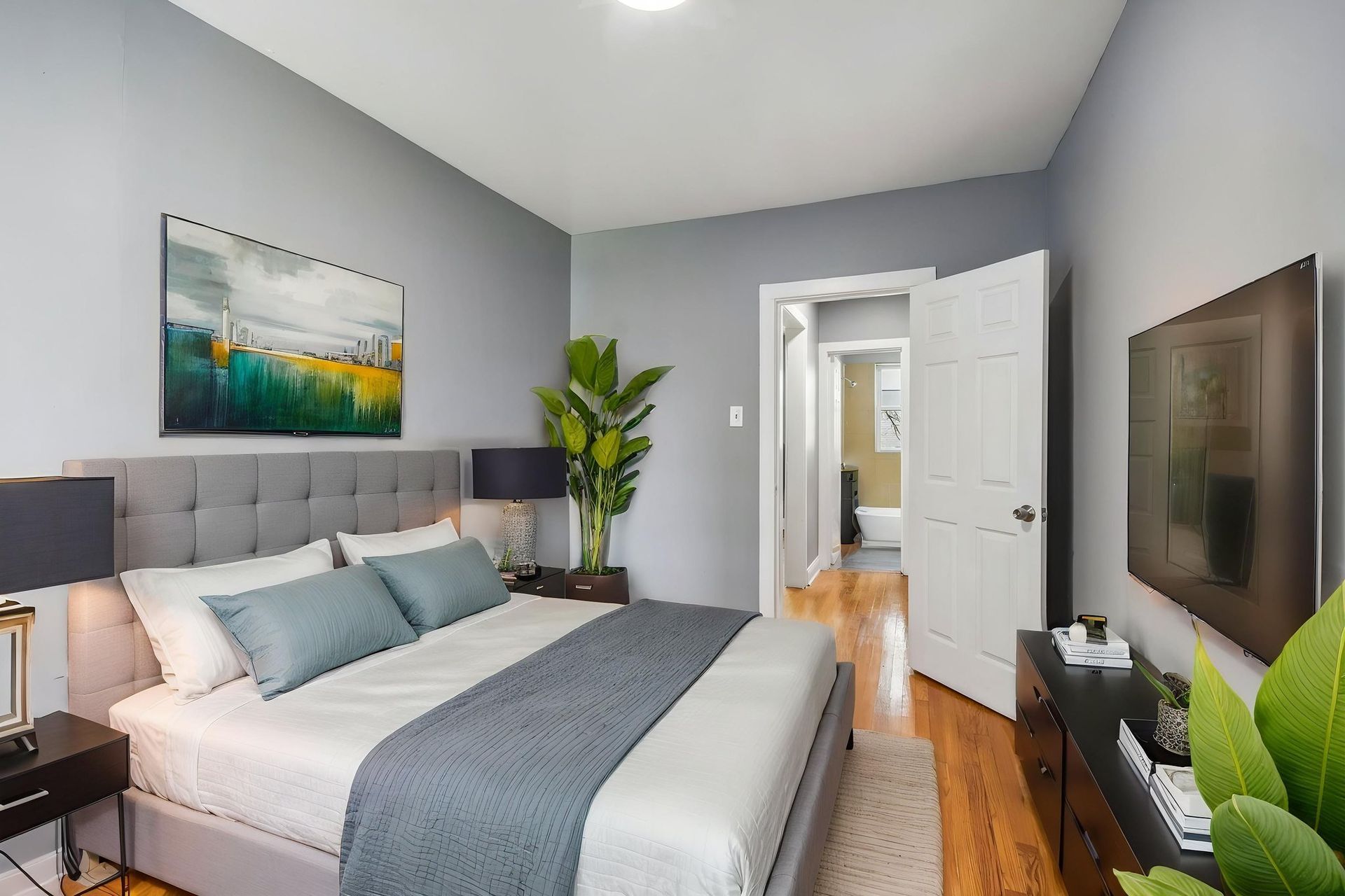 Modern bedroom with gray walls, upholstered bed, teal pillows, wall art, and an open door to a hallway