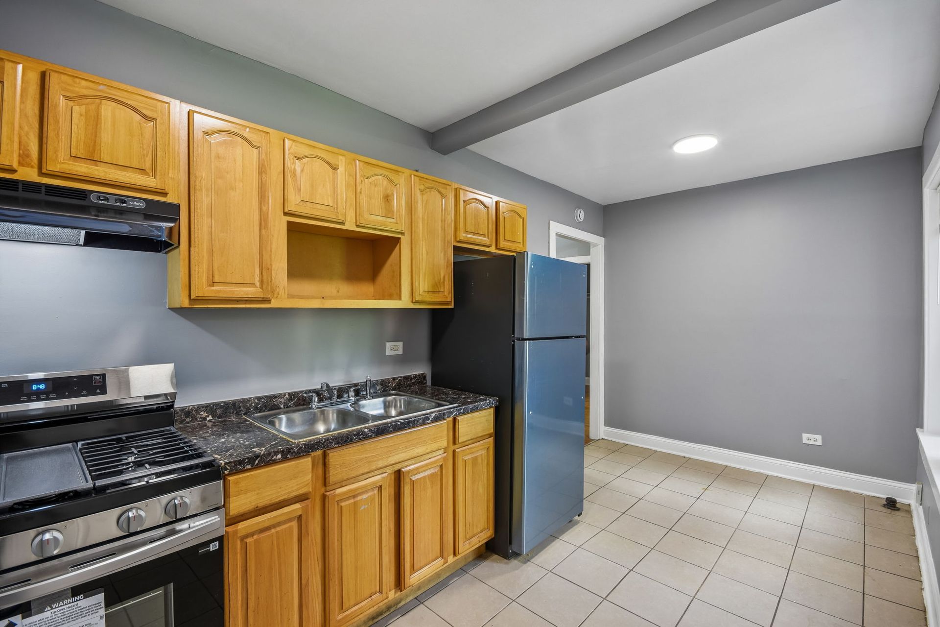 Small kitchen with wood cabinets, black stove, blue refrigerator, and tiled floor in a gray room