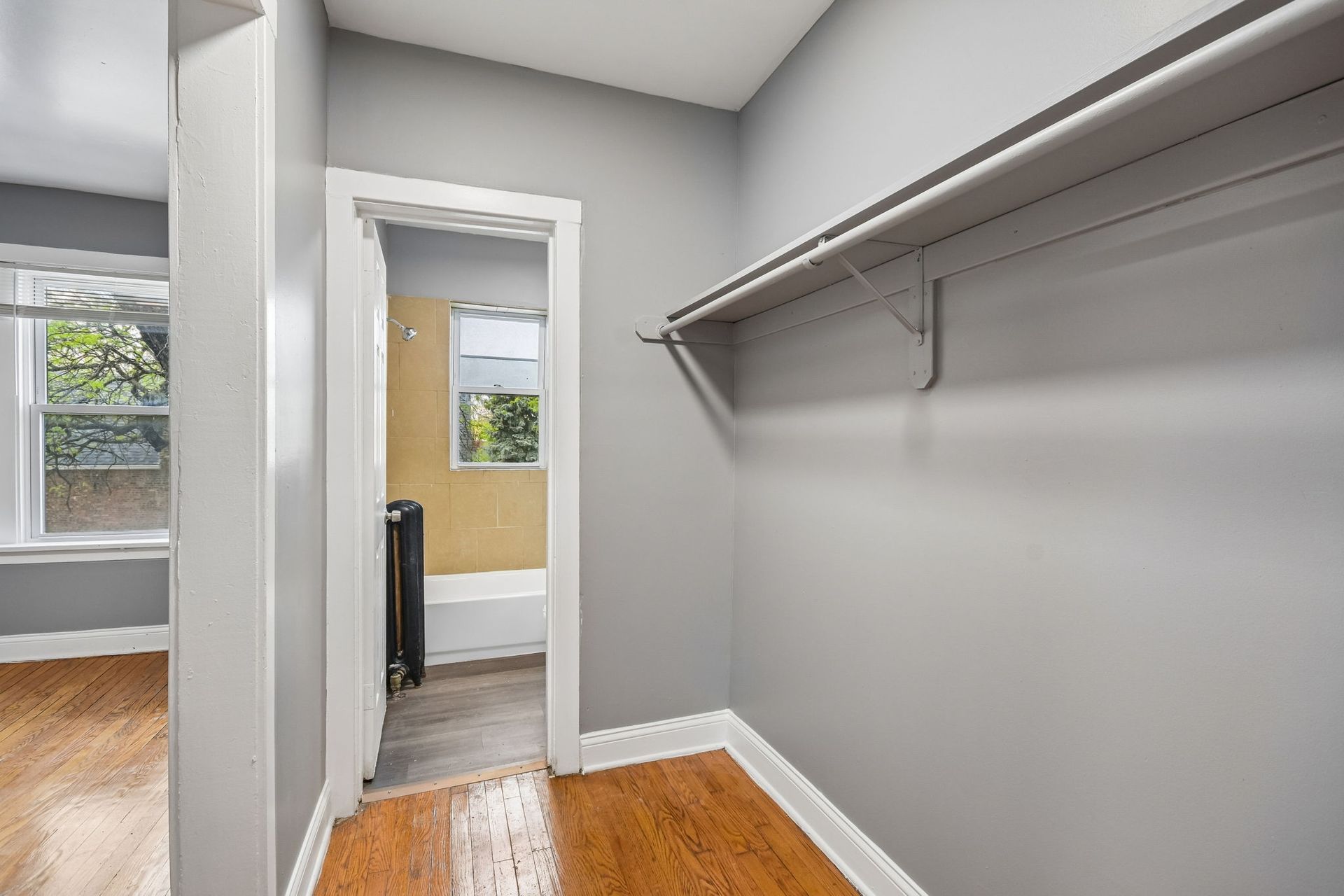 Empty walk-in closet with gray walls, wood floor, and built-in shelves, viewed toward a doorway.