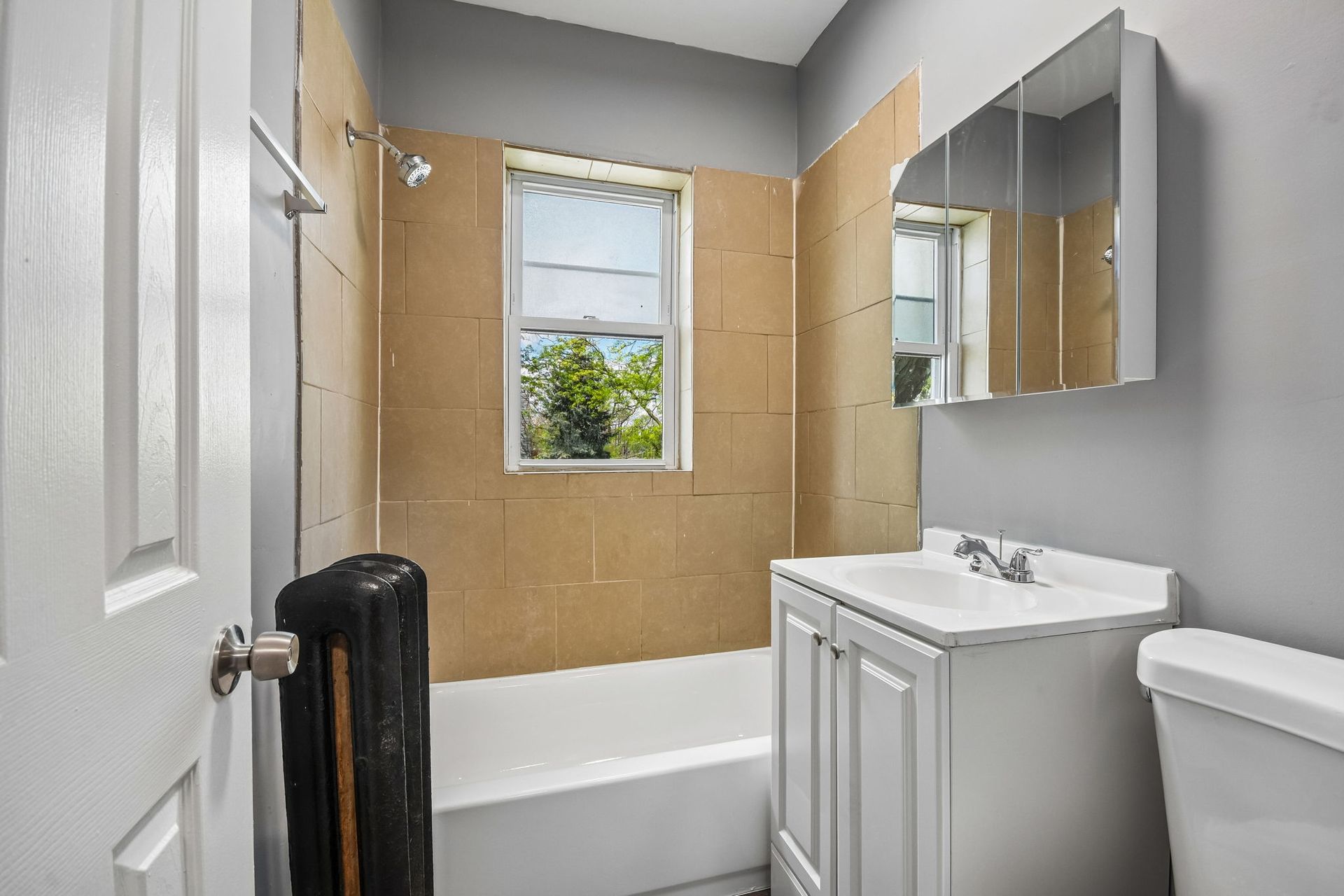 Small bathroom with tub, sink vanity, mirror cabinet, and a window showing greenery.