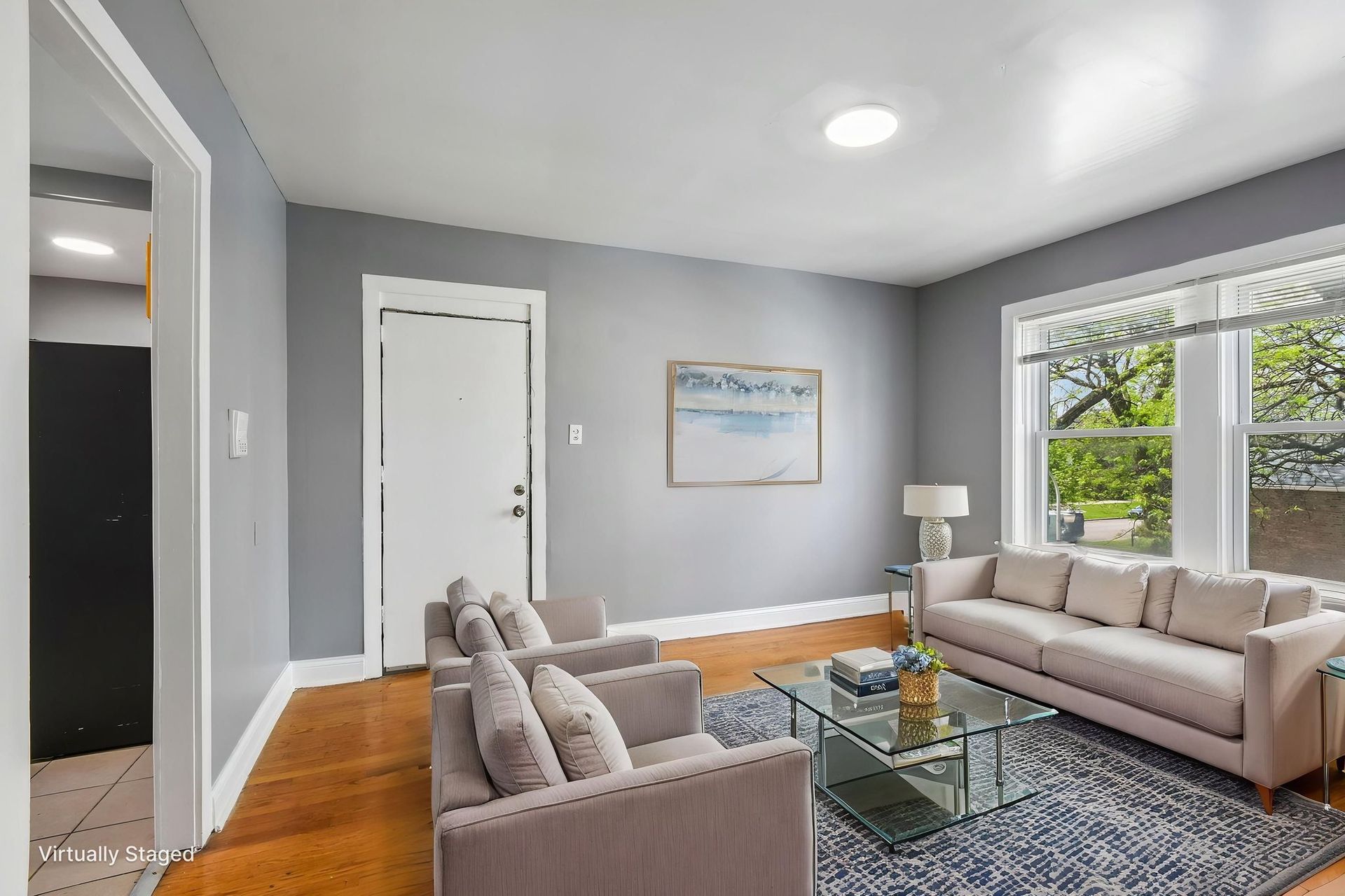 Bright living room with gray walls, beige sofas, glass coffee table, and large window view