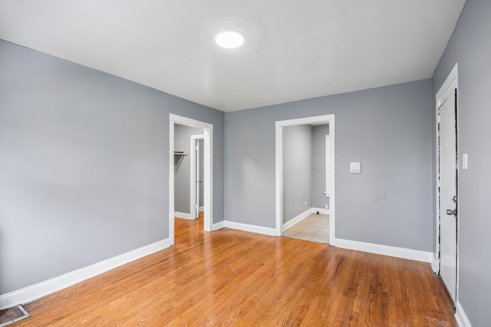 Empty gray room with hardwood floors, white trim, and two open doorways.
