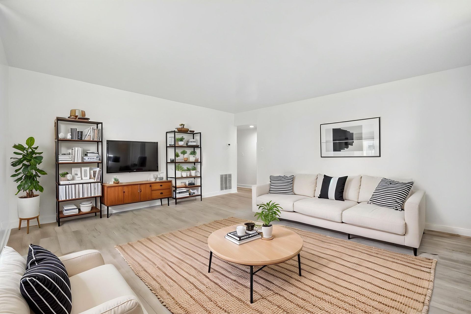 Bright minimalist living room with white sofa, TV, wooden console, shelving, and woven rug