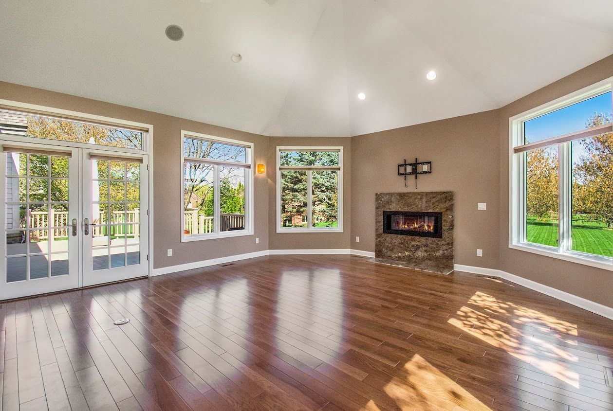 Bright empty living room with hardwood floors, fireplace, and large windows letting in sunlight