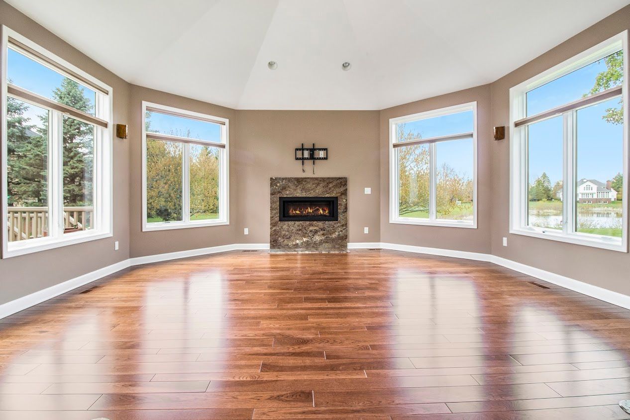 Bright empty living room with hardwood floors, large windows, and a fireplace centered on the far wall