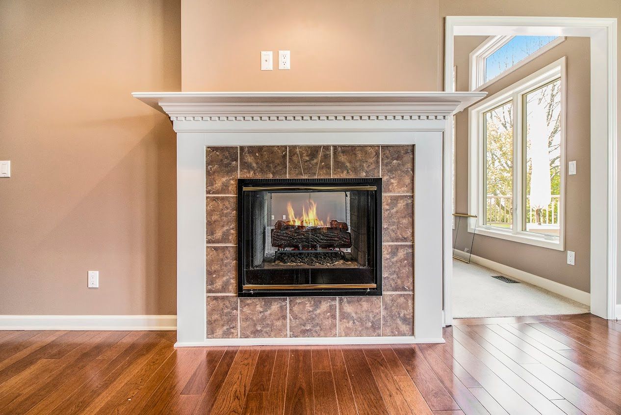 Living room fireplace with stone surround, wood floor, and bright windows at right