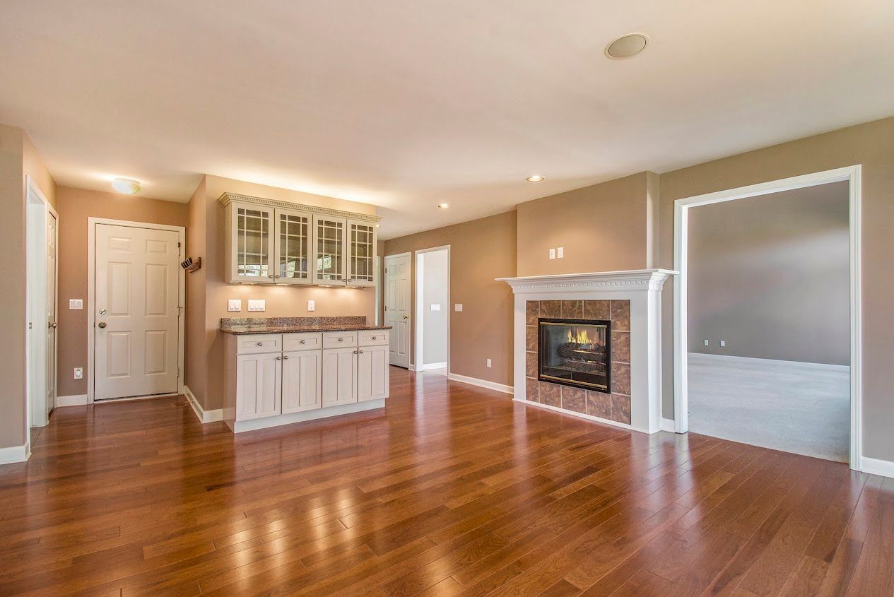 Spacious beige living room with hardwood floors, white fireplace, and a built-in cabinet nook.