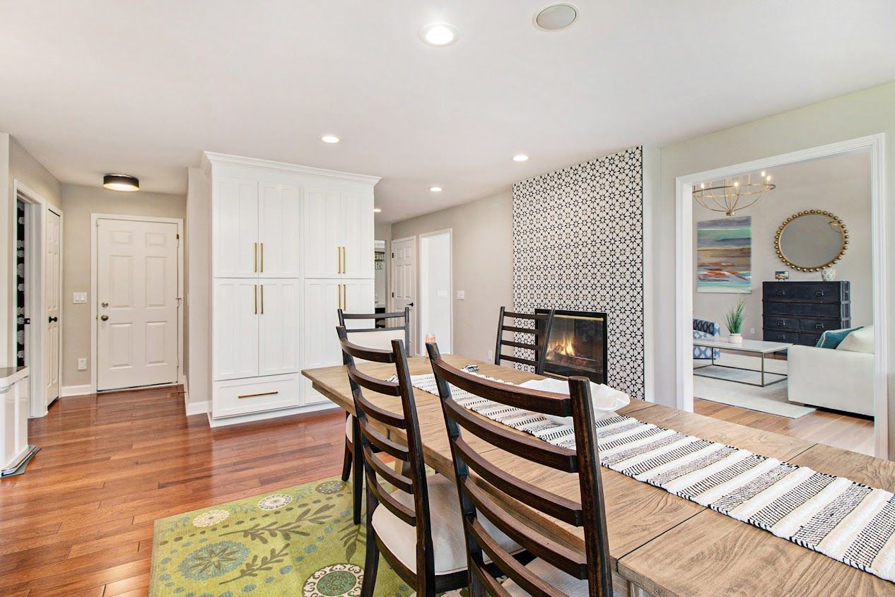 Bright dining room with wooden table, patterned chairs, white cabinets, and a large wall mirror.
